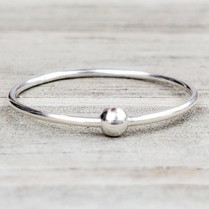 May include: A simple silver ring with a smooth, round bead in the center.