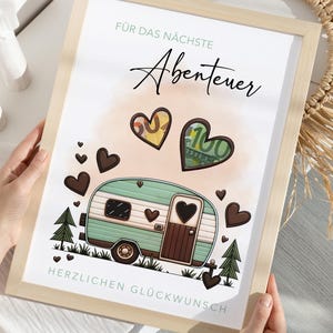 May include: A framed print with a light wood frame. The print features a teal and brown camper illustration with heart accents, money-filled hearts, and the German text "F&uuml;r das n&auml;chste Abenteuer" and "Herzlichen Gl&uuml;ckwunsch".