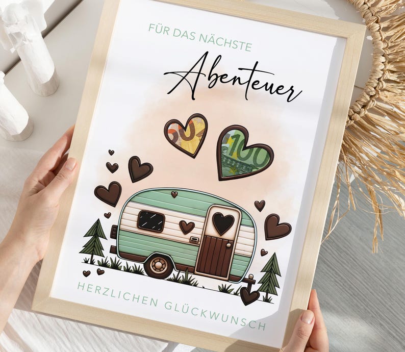 May include: A framed print with a light wood frame. The print features a teal and brown camper illustration with heart accents, money-filled hearts, and the German text "F&uuml;r das n&auml;chste Abenteuer" and "Herzlichen Gl&uuml;ckwunsch".