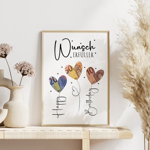 Gerahmtes Bild mit der Aufschrift „Wunscherfüller“ in stilvoller, schwarzer Schrift. Darunter drei herzförmige Ballons, gestaltet aus gefalteten Euro-Geldscheinen (20, 50 und 10 Euro). Die Ballons sind mit feinen Linien verbunden, daneben steht „Happy Birthday“ in verschnörkelter Schrift. Kleine Sterne verzieren das Design auf weißem Hintergrund.