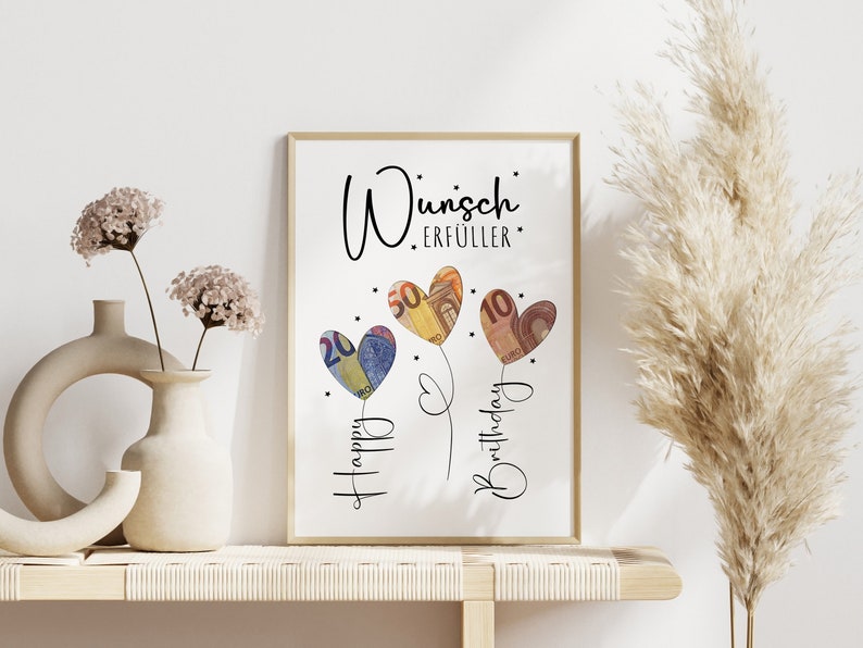 Gerahmtes Bild mit der Aufschrift „Wunscherfüller“ in stilvoller, schwarzer Schrift. Darunter drei herzförmige Ballons, gestaltet aus gefalteten Euro-Geldscheinen (20, 50 und 10 Euro). Die Ballons sind mit feinen Linien verbunden, daneben steht „Happy Birthday“ in verschnörkelter Schrift. Kleine Sterne verzieren das Design auf weißem Hintergrund.