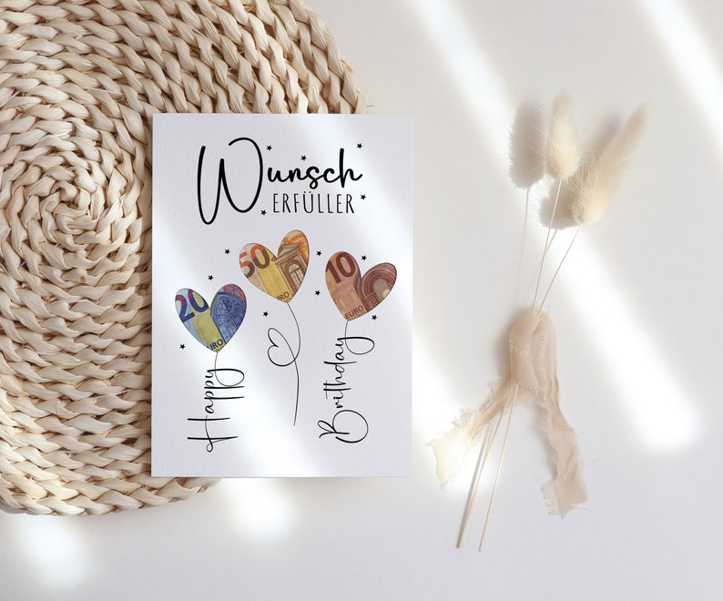 Bild mit der Aufschrift „Wunscherfüller“ in stilvoller, schwarzer Schrift. Darunter drei herzförmige Ballons, hinterlegt mit Euro-Geldscheinen (20, 50 und 10 Euro). Die Ballons sind mit feinen Linien verbunden, darunter steht „Happy Birthday“ in verschnörkelter Schrift. Kleine Sterne verzieren das Design auf weißem Hintergrund.