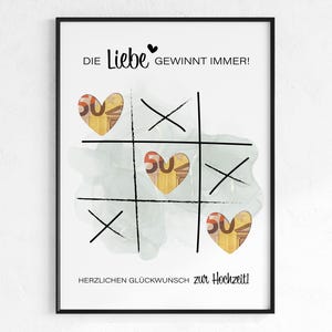 Può includere: Stampa incorniciata con un design del gioco tris. Il tabellone presenta elementi a forma di cuore con il numero 50 all'interno. Il testo in alto recita "Die Liebe gewinnt immer!" e in basso "Herzlichen Glückwunsch zur Hochzeit!"