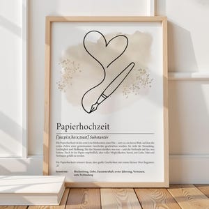 K&ouml;nnte beinhalten: Ein gerahmter Kunstdruck mit einem minimalistischen Design aus Herz und Stift, mit dem deutschen Wort "Papierhochzeit" unten. Das Kunstwerk hat eine neutrale Farbpalette mit beige und schwarzen Elementen, passend f&uuml;r die Inneneinrichtung.