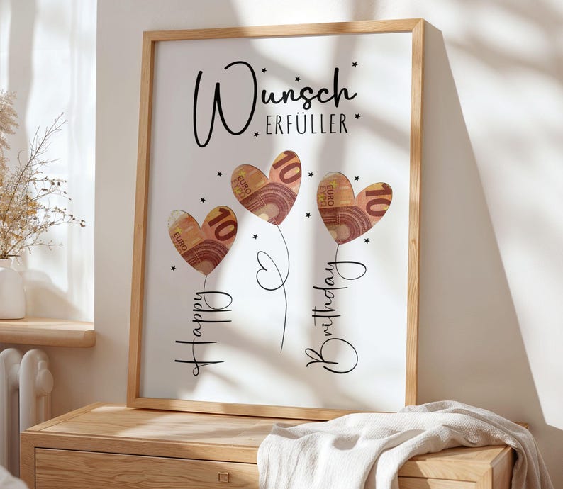 May include: A framed print with a light wood frame. The artwork features three heart-shaped balloons made of Euro banknotes, each with a "10" printed on them. The words "Happy Birthday" and "Wunsch Erf&uuml;ller" are written in black script.