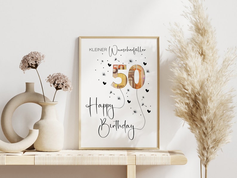 May include: A white framed print with the text "KLEINER Wunscherefaller" and "Happy Birthday" with a 50 euro bill shaped like a dandelion.