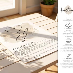K&ouml;nnte beinhalten: Beiger Druck mit einer Herz- und Feder-Illustration, dem deutschen Wort &bdquo;Papierhochzeit&ldquo; (Papierhochzeit) und Text. Der Druck befindet sich auf einem hellen Holztisch, mit einer Pflanze in einem Terrakotta-Topf im Hintergrund.