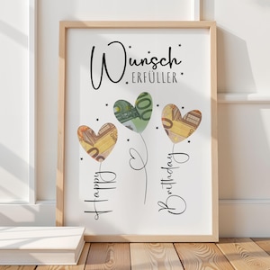 May include: A framed print with the words "Wunsch Erf&uuml;ller" and "Happy Birthday" in script. Three heart-shaped balloons are filled with Euro banknotes. The frame is light brown, and the background is white.