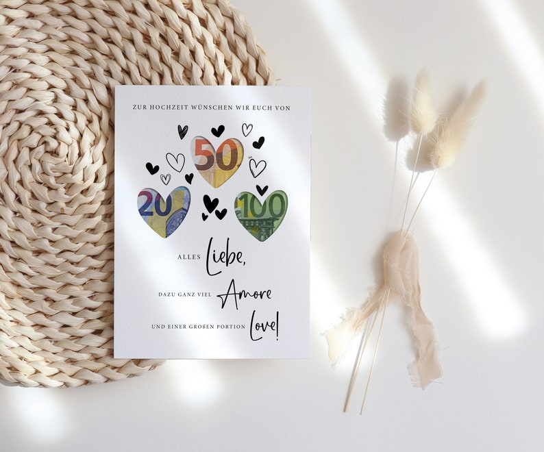 May include: A white card with black hearts and the words "Zur Hochzeit w&uuml;nschen wir euch von" at the top. The hearts are filled with euro bills. The text below the hearts reads "Alles Liebe, Amore Love!" with the words "dazu ganz viel" and "und einer gro&szlig;en Portion" below.