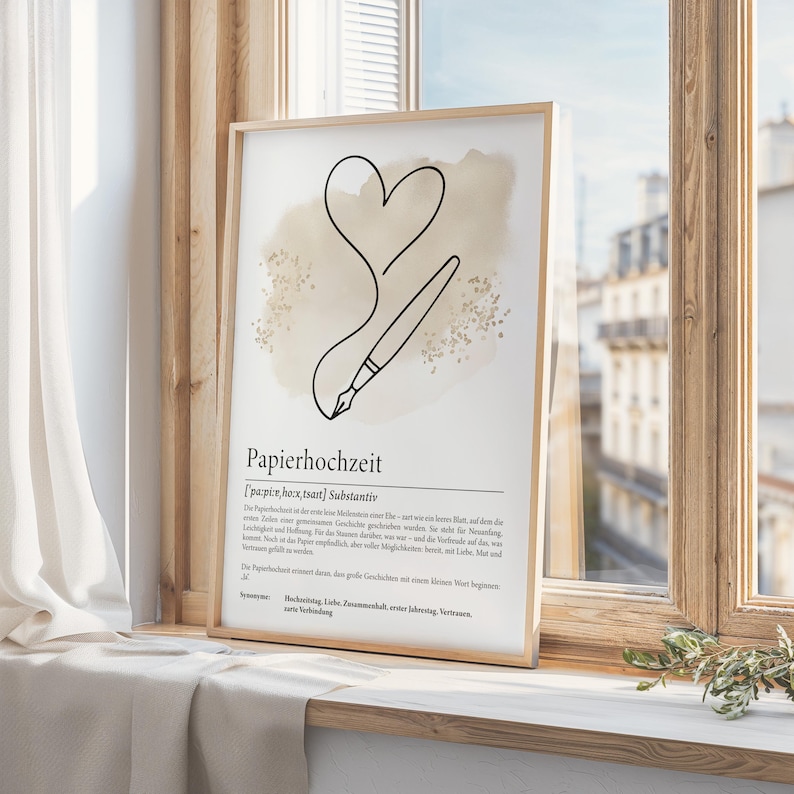 K&ouml;nnte beinhalten: Ein gerahmter Druck mit einer minimalistischen Strichzeichnung eines Herzens und eines Stifts, mit dem deutschen Wort "Papierhochzeit" unten. Das Kunstwerk hat eine neutrale Farbpalette mit beigem Hintergrund und wird auf einer Fensterbank ausgestellt.