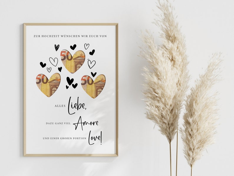May include: A white card with a gold frame, featuring a heart-shaped design with money inside. The card has the text "Zur Hochzeit w&uuml;nschen wir euch von Alles Liebe, Amore und einer gro&szlig;en Portion Love!"