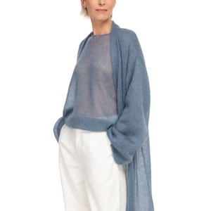 May include: A woman wearing a light blue, sheer knit sweater and a matching long cardigan. She is also wearing white pants. The clothing appears to be made of a soft, lightweight material. The background is plain white.