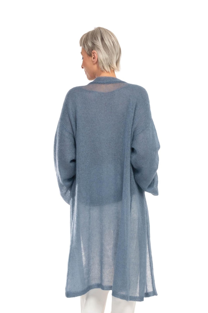 May include: A long, light blue cardigan with long sleeves. The cardigan is made of a sheer, open-knit fabric. The model is wearing the cardigan over a white top and pants. The cardigan falls to the mid-calf.