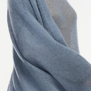 May include: A light blue knit cardigan with long sleeves. The cardigan is made of a soft, sheer material and drapes over a light gray top. The knitwear has a loose weave, creating a delicate texture. The overall style is casual and comfortable.