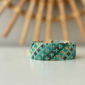 May include: A turquoise, brown and gold beaded bracelet with a geometric pattern.