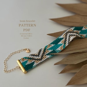 Può includere: Un braccialetto in tessuto a telaio turchese, bianco, oro e grigio con una chiusura dorata. Il braccialetto è lungo 14,86 cm e largo 1,75 cm. Il motivo è geometrico e include un design a chevron. Il braccialetto è realizzato con 6 colori di perline.