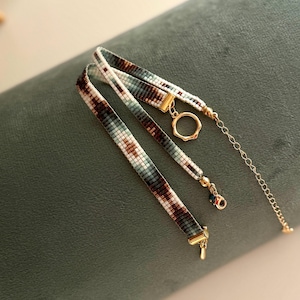 May include: Two layered beaded necklaces with a white, brown, and blue geometric pattern. The necklaces have gold clasps and a gold ring connector.