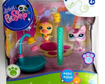 May include: A Littlest Pet Shop playset with a pink and yellow duck and a white cat with pink ears and a sparkly crown. The set includes a blue shower, a pink and white striped towel, and a pink and green polka dot rug. The box has the Littlest Pet Shop logo and the number 36368.
