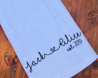 Peut inclure: Une serviette de cuisine bleu clair avec une broderie noire qui dit "Jack & Alice est. 2019".