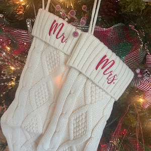 May include: A pair of white knitted Christmas stockings with red embroidered text, one saying "Mr." and the other saying "Mrs."
