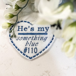 May include: White felt heart-shaped patch with blue embroidered text that reads "He's my something blue #110".
