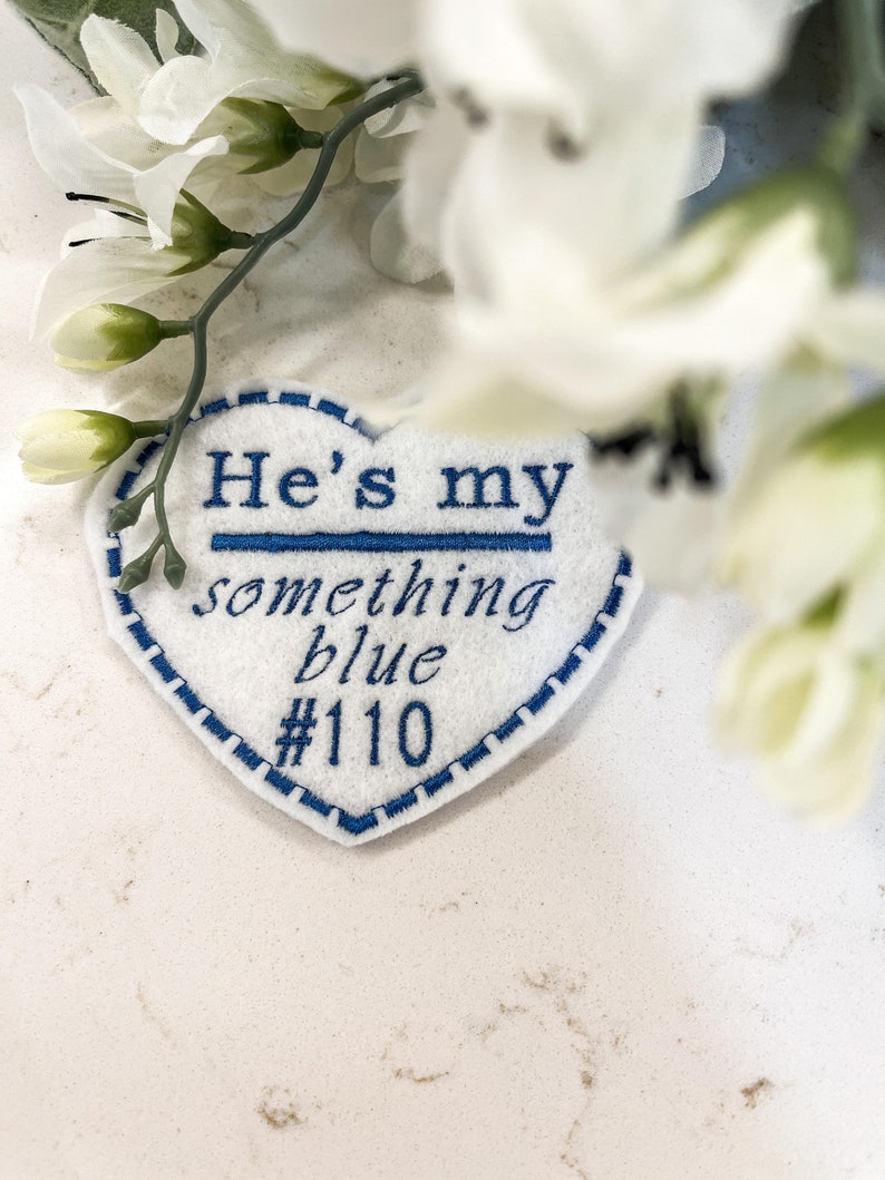 May include: White felt heart-shaped patch with blue embroidered text that reads "He's my something blue #110".
