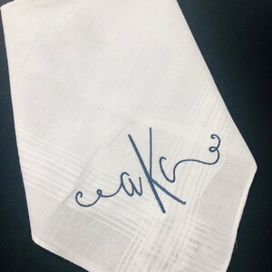 May include: White handkerchief with a subtle plaid pattern. The handkerchief features embroidered initials in a cursive font, using navy blue thread. The initials appear to be "aKc".