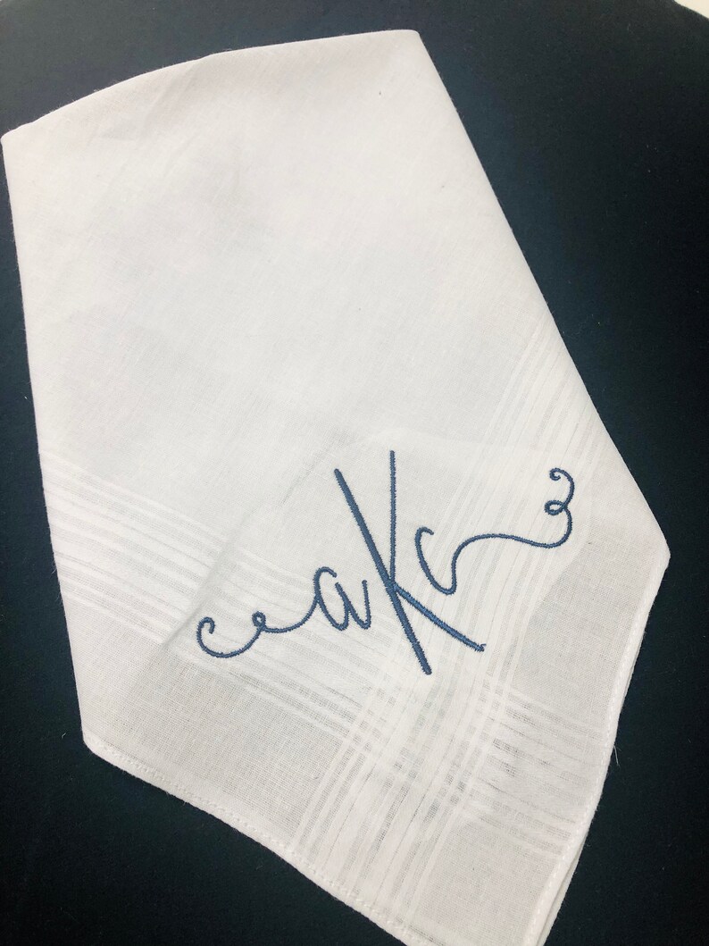 May include: White handkerchief with a subtle plaid pattern. The handkerchief features embroidered initials in a cursive font, using navy blue thread. The initials appear to be "aKc".