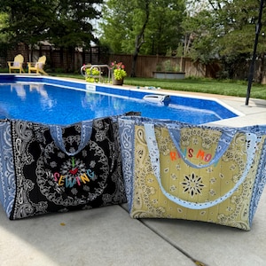 May include: Two quilted tote bags featuring paisley bandana patterns. The black bag displays the embroidered text "I love sewing" with a red heart. The yellow bag features the embroidered text "RINS MO" in orange and red letters with blue handles.