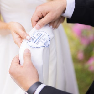 May include: A white wedding dress with a blue heart-shaped patch sewn on the side that says "He's my something blue #392".