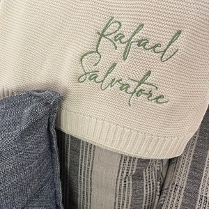May include: A cream-colored knitted baby blanket with the name "Rafael Salvatore" embroidered in green.