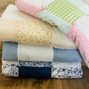 May include: A stack of patchwork quilt squares in various patterns and colors, including pink, green, blue, white, and floral prints. The squares are sewn together to create a unique and colorful quilt.