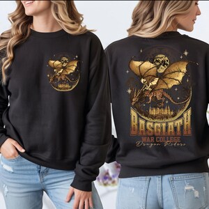 a woman wearing a black sweatshirt with a graphic design on the back. The design includes a golden dragon and stars, along with the text "BASGIATH WAR COLLEGE Dragon Riders".