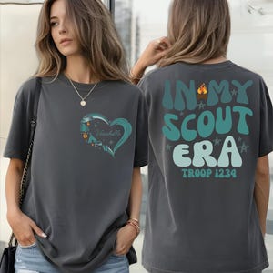 A woman wearing a gray t-shirt with a heart design and text on the back.