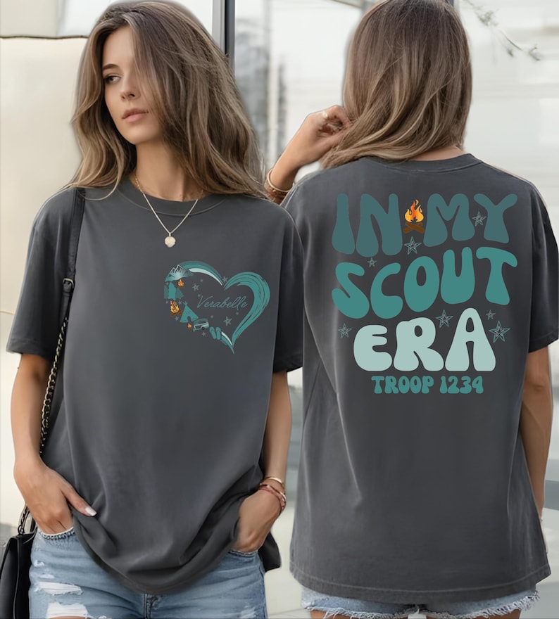 A woman wearing a gray t-shirt with a heart design and text on the back.
