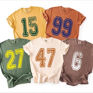 a collection of five t-shirts, each with a different number printed on it.