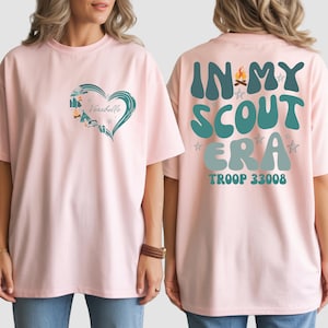 A woman wearing a pink t-shirt with a heart design and text on the back.