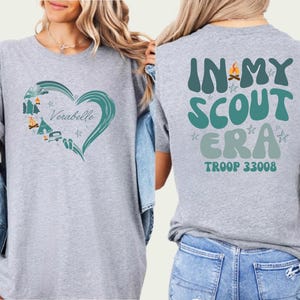 A woman wearing a gray t-shirt with a heart design and text on the back.