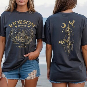 Two women wearing black t-shirts with gold designs on them, standing on a beach.