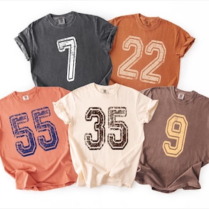 a collection of five t-shirts, each with a different number printed on them.