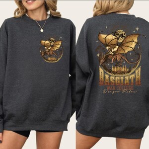 a gray sweatshirt with a graphic design on the back. The design depicts a dragon and a castle, with the text "BASGIATH Dragon Riders" written below the dragon.