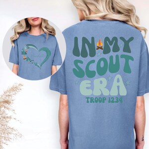 A woman wearing a blue t-shirt with the text "IN MY SCOUT ERA" printed on it.