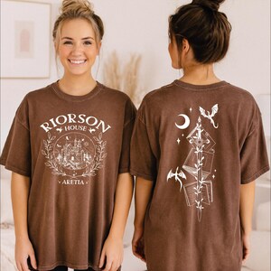 A woman wearing a brown t-shirt with a graphic design on the front and back.