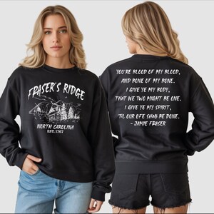 A woman wearing a black sweatshirt with text and graphics printed on it.