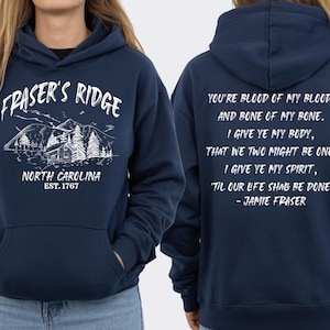A navy blue hoodie with white text and graphics, including a mountain landscape and a quote.
