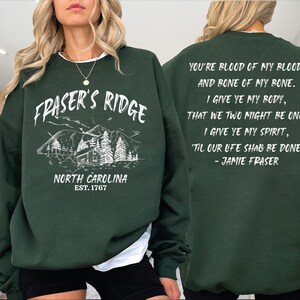 A woman wearing a green sweatshirt with text and a mountain illustration on it.