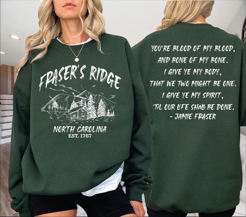 A woman wearing a green sweatshirt with text and a mountain illustration on it.