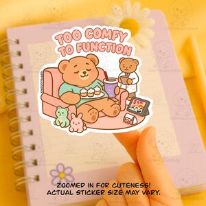 May include: A sticker featuring a cartoon bear relaxing on a couch with cupcakes and a drink, with the text "TOO COMFY TO FUNCTION". A smaller bear in a lab coat and other cute characters are also shown.