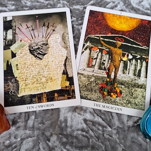 Puede incluir: Dos cartas de tarot, Diez de Espadas y El Mago, se muestran sobre una superficie gris texturizada. Tambi&eacute;n se muestra una piedra marr&oacute;n y un escarabajo azul.