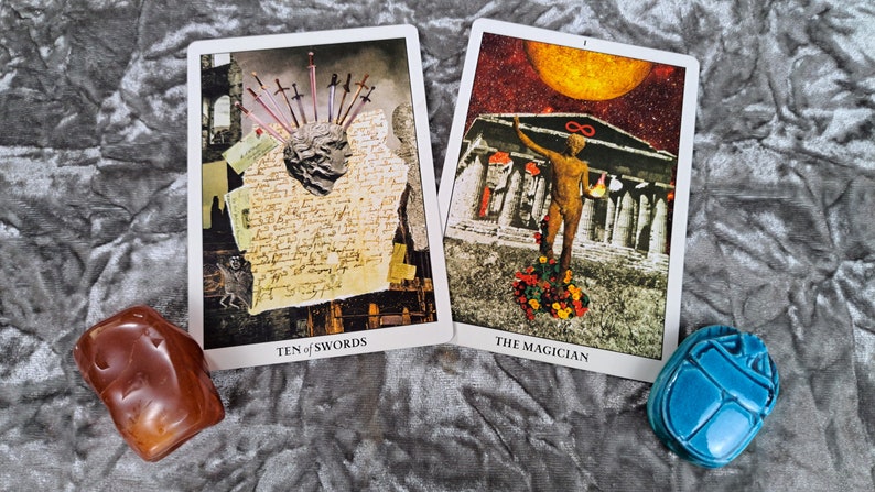 Puede incluir: Dos cartas de tarot, Diez de Espadas y El Mago, se muestran sobre una superficie gris texturizada. Tambi&eacute;n se muestra una piedra marr&oacute;n y un escarabajo azul.